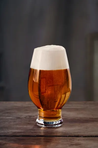 Tulipformet glas med ravfarvet øl og tykt hvidt skum på et rustikt træbord.