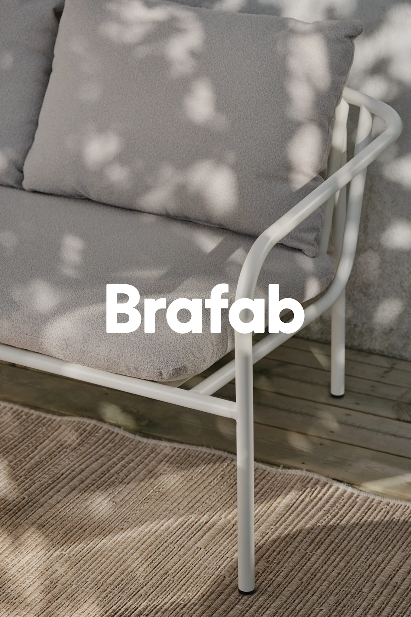 Brafab-logo over en lysegrå udendørssofa med hvid metalramme, på beige tæppe på træterrasse med skygger.