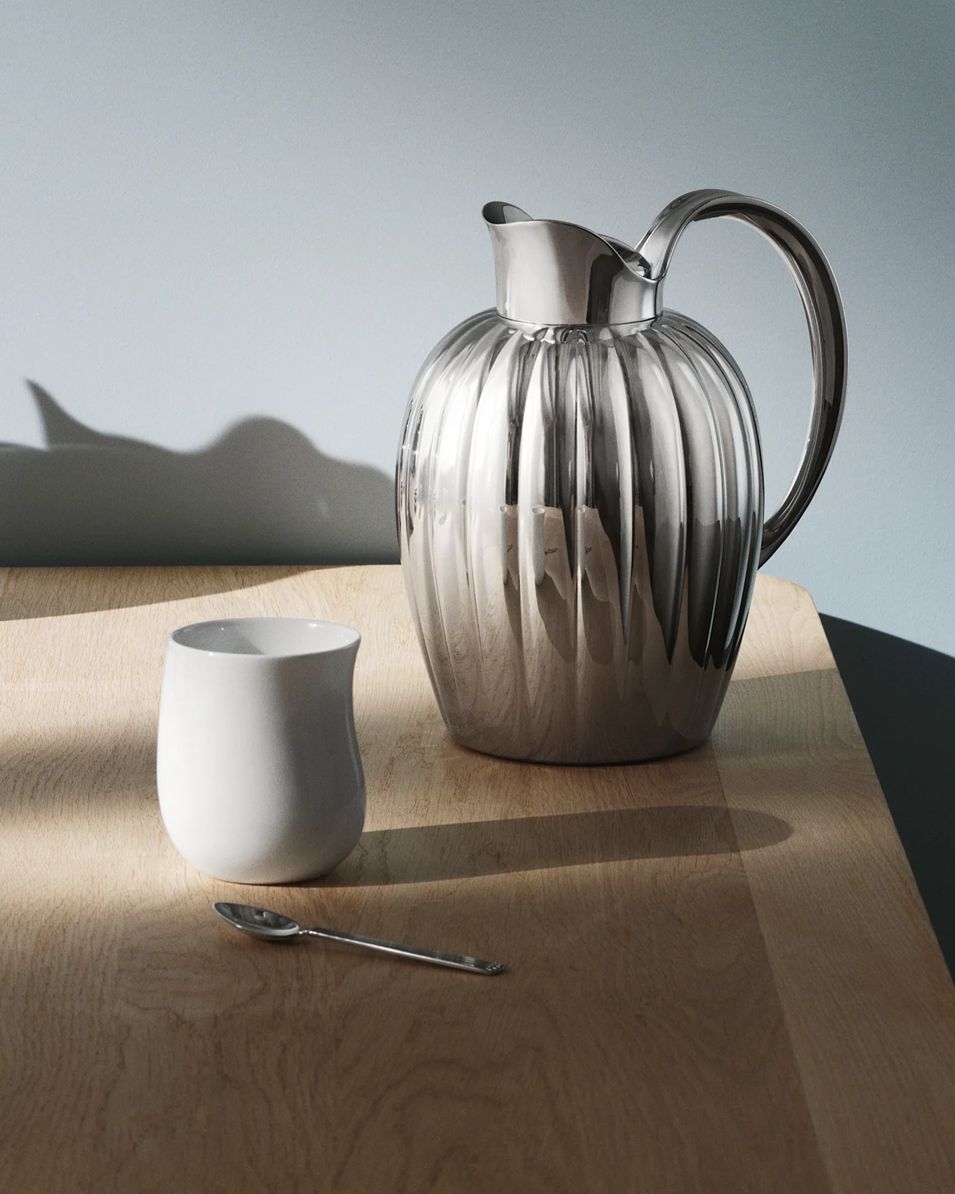 En skinnende, riflet sølvkande med et håndtag står på et mørkt, reflekterende bord, med lysmønstre kastet over overfladen.