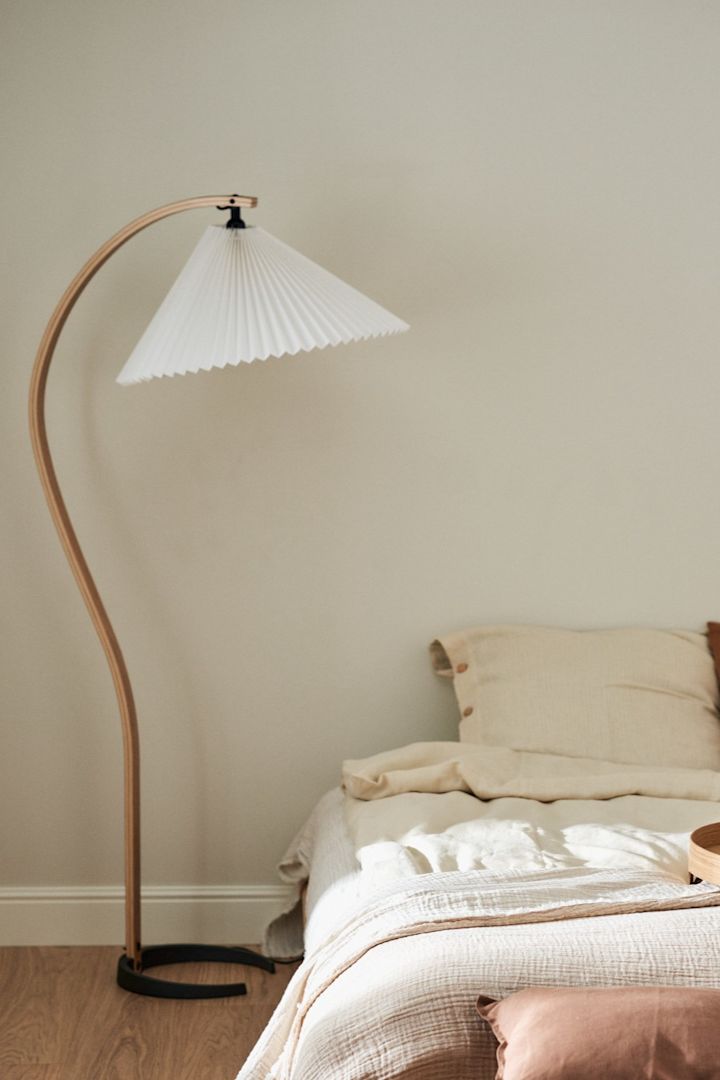 Opfrisk dit hjem med disse moderne belysningsideer. Her ser du Gubi Timberline-gulvlampen med det buede træben, der står ved siden af en seng. 