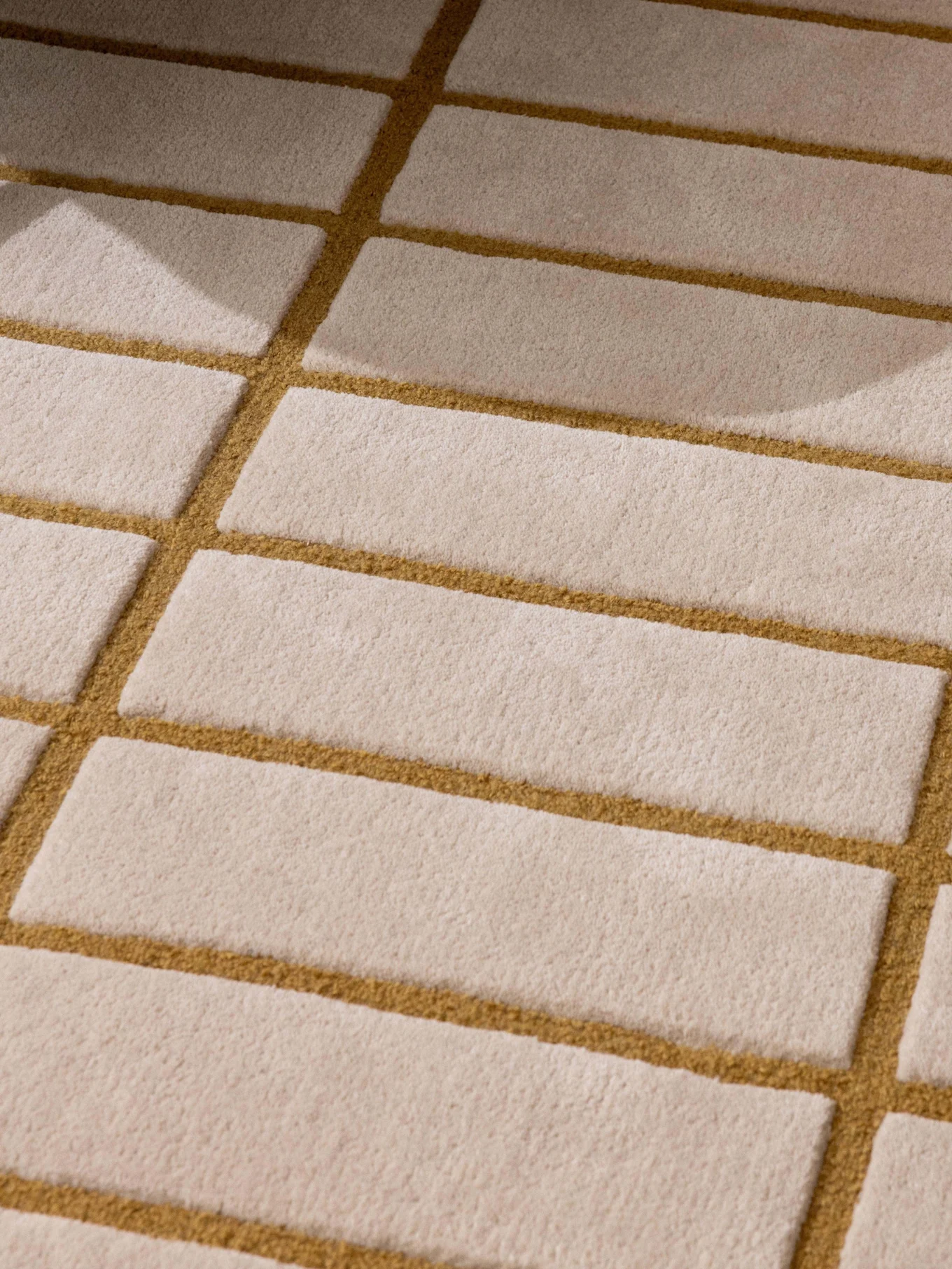 Mønstret beige og gyldenbrunt tæppe, grønt lænestolsben og en bakke med en hvid tekande og kop.