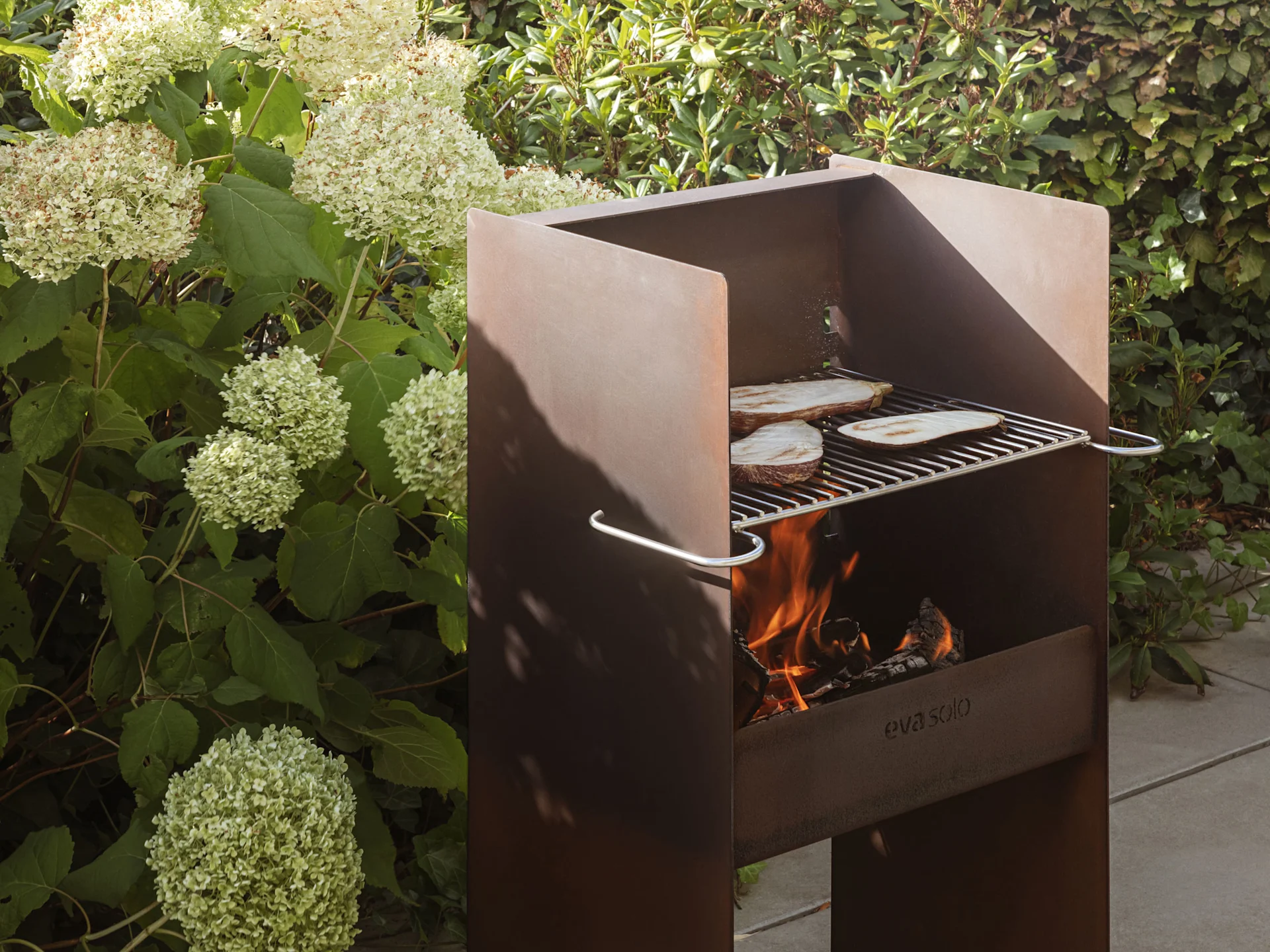 En rustik metaludendørsgrill med flammer og aubergineskiver, der steger på risten.