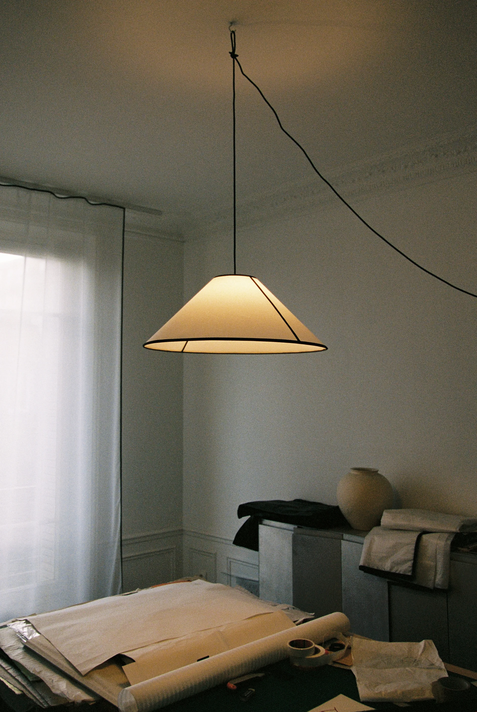 Et hyggeligt rum med en cremefarvet lodden lænestol, en beige justerbar gulvlampe og en mørk træhylde med kunst og bøger.