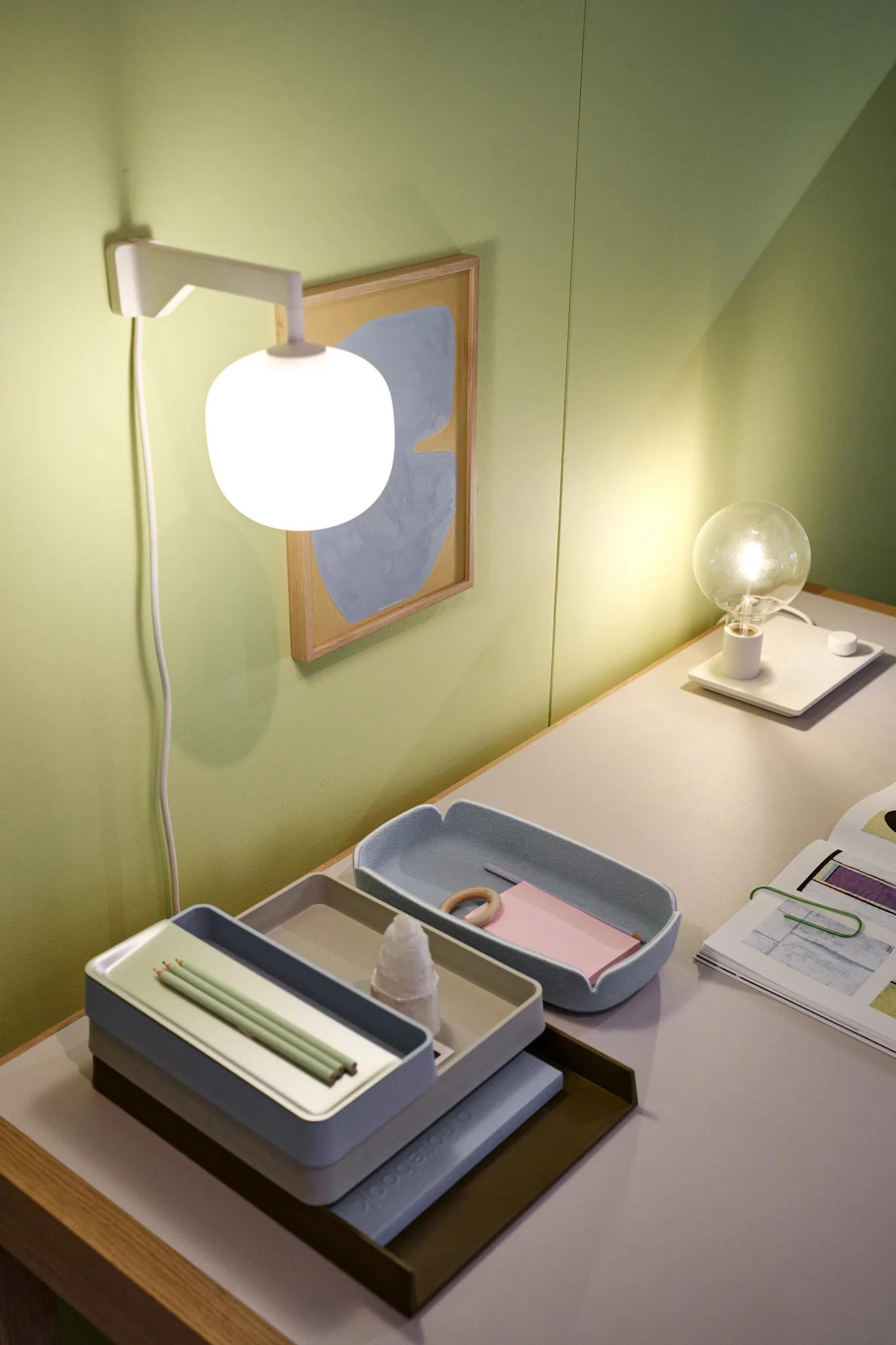 Et pænt skrivebord foran en grøn væg med den beigefarvede Rime-væglampe fra Muuto.