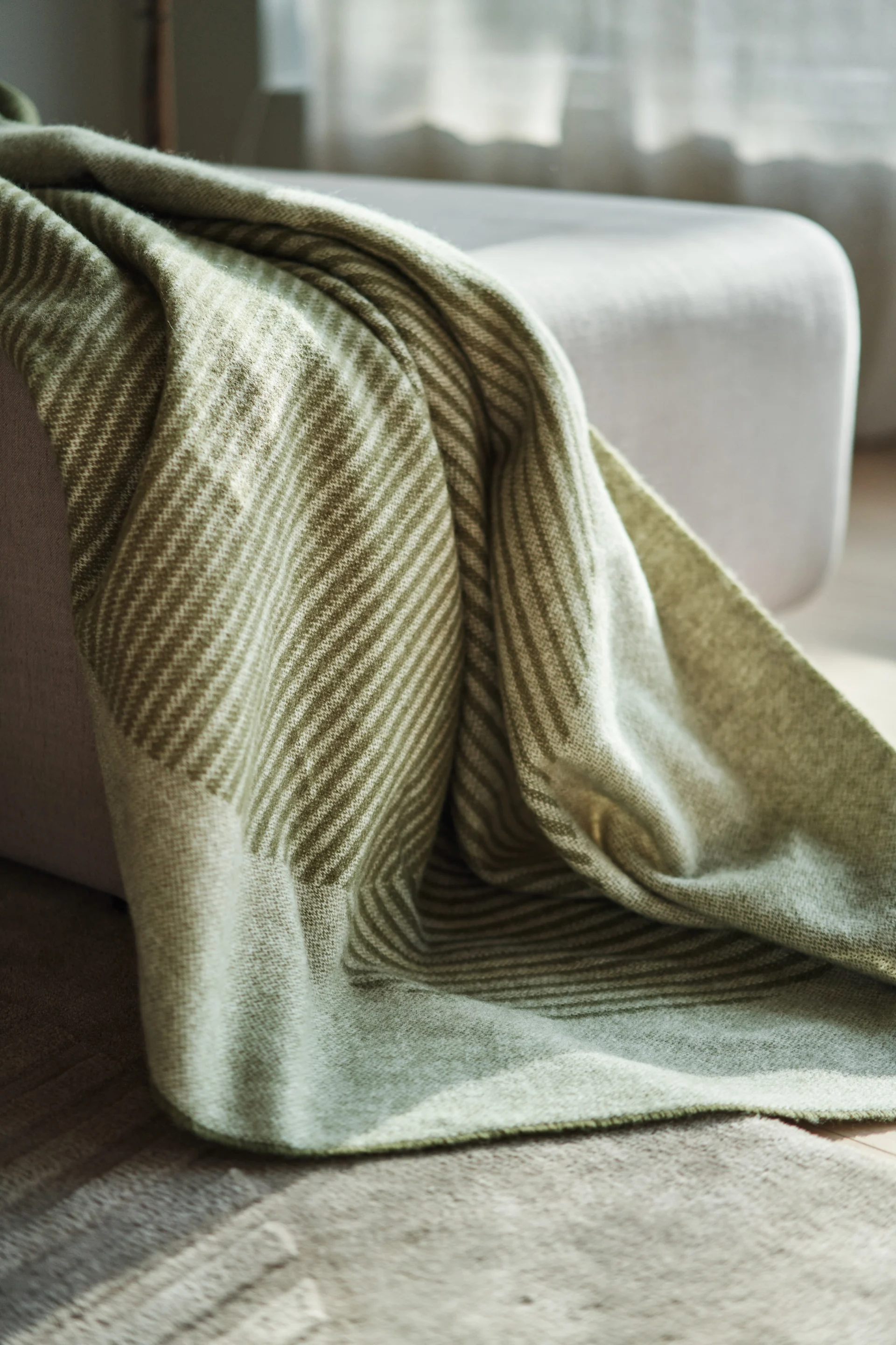 Et lækker, blød Circles uldplaid i grøn fra NJRD ses her læggende på en seng. Dette er en nem måde at bringe naturen ind i dit hjem. 