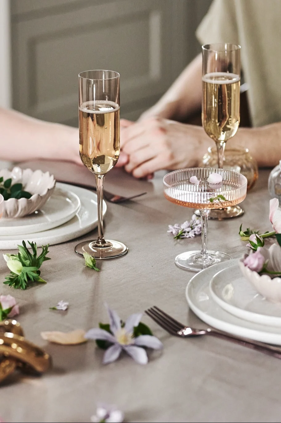 Du kan også pynte bordet på en legende måde til dit romantiske måltid derhjemme. Her ser du hvidt service, enkle glas og blomster på en beigefarvet dug.