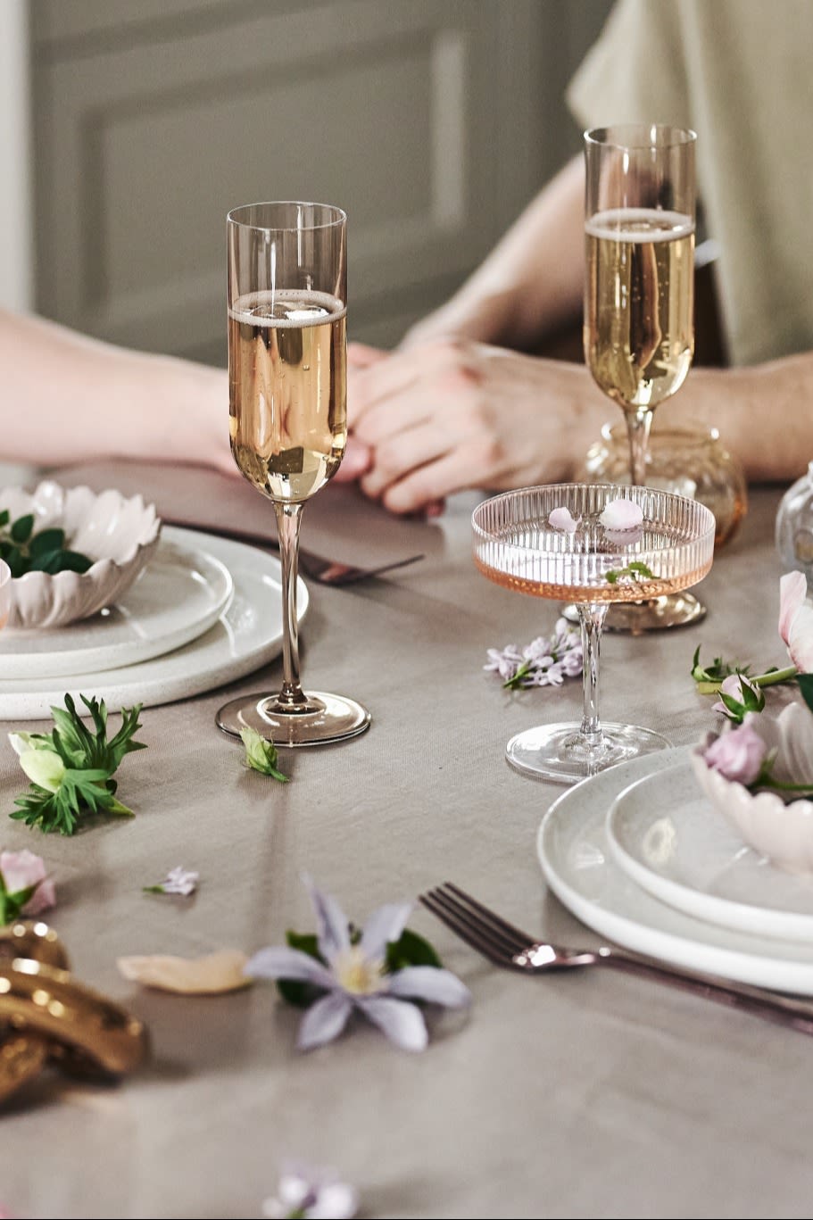 Du kan også pynte bordet på en legende måde til dit romantiske måltid derhjemme. Her ser du hvidt service, enkle glas og blomster på en beigefarvet dug.