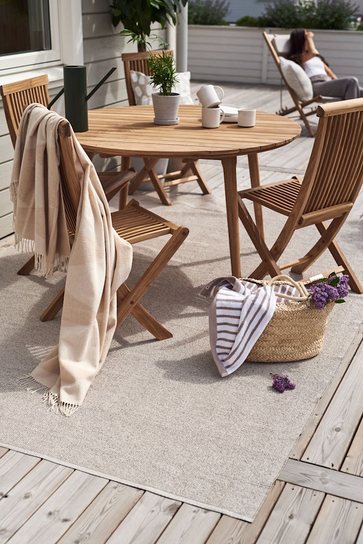 En terrasse med træmøbler, for eksempel Aneboda-balkonsættet fra 1898 og Rime-bomuldstæppet fra Scandi Living på Mellow-plasttæppet.
