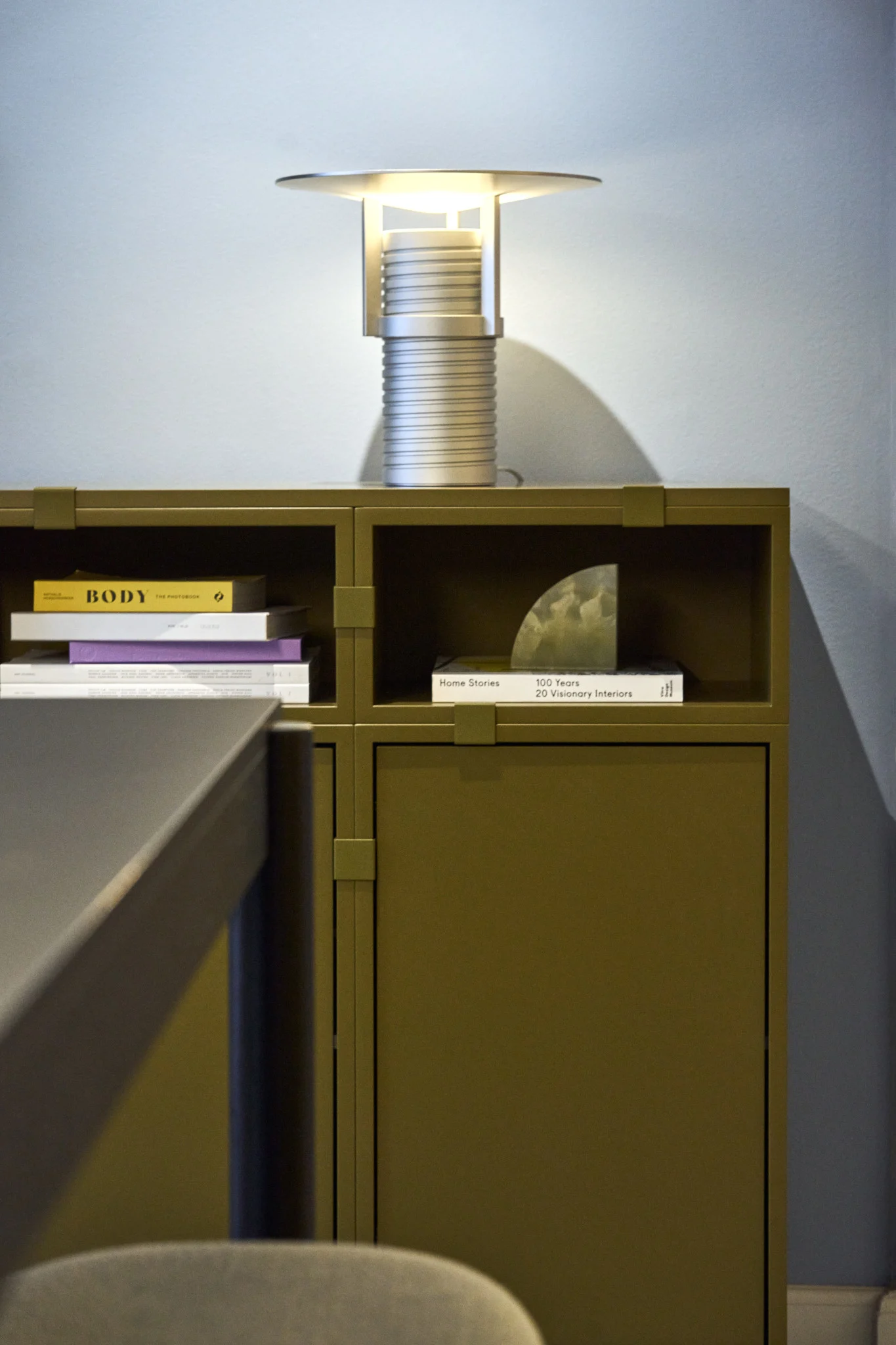 En grøn hylde, bygget af Stacked-kollektionen, med den sølvfarvede Set-bordlampe ovenpå, alt sammen fra Muuto.