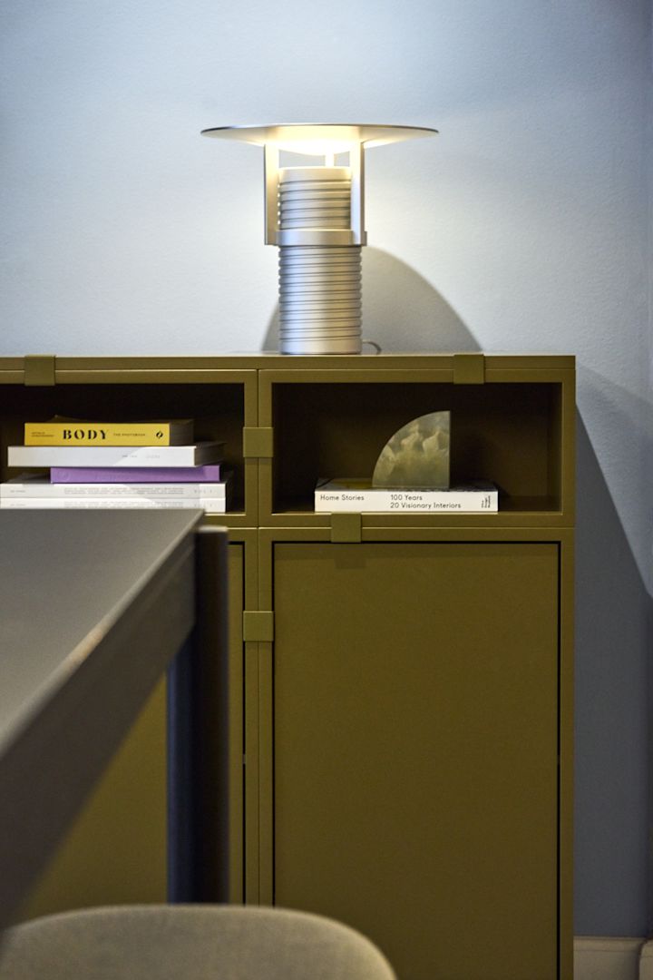 En grøn hylde, bygget af Stacked-kollektionen, med den sølvfarvede Set-bordlampe ovenpå, alt sammen fra Muuto.