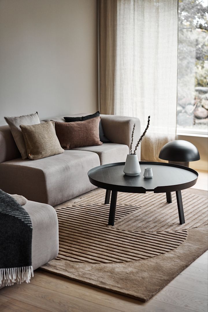Indret med hyggelige tæpper til din stue - her ses det beige Circles uldtæppe fra NJRD i en beige stue.