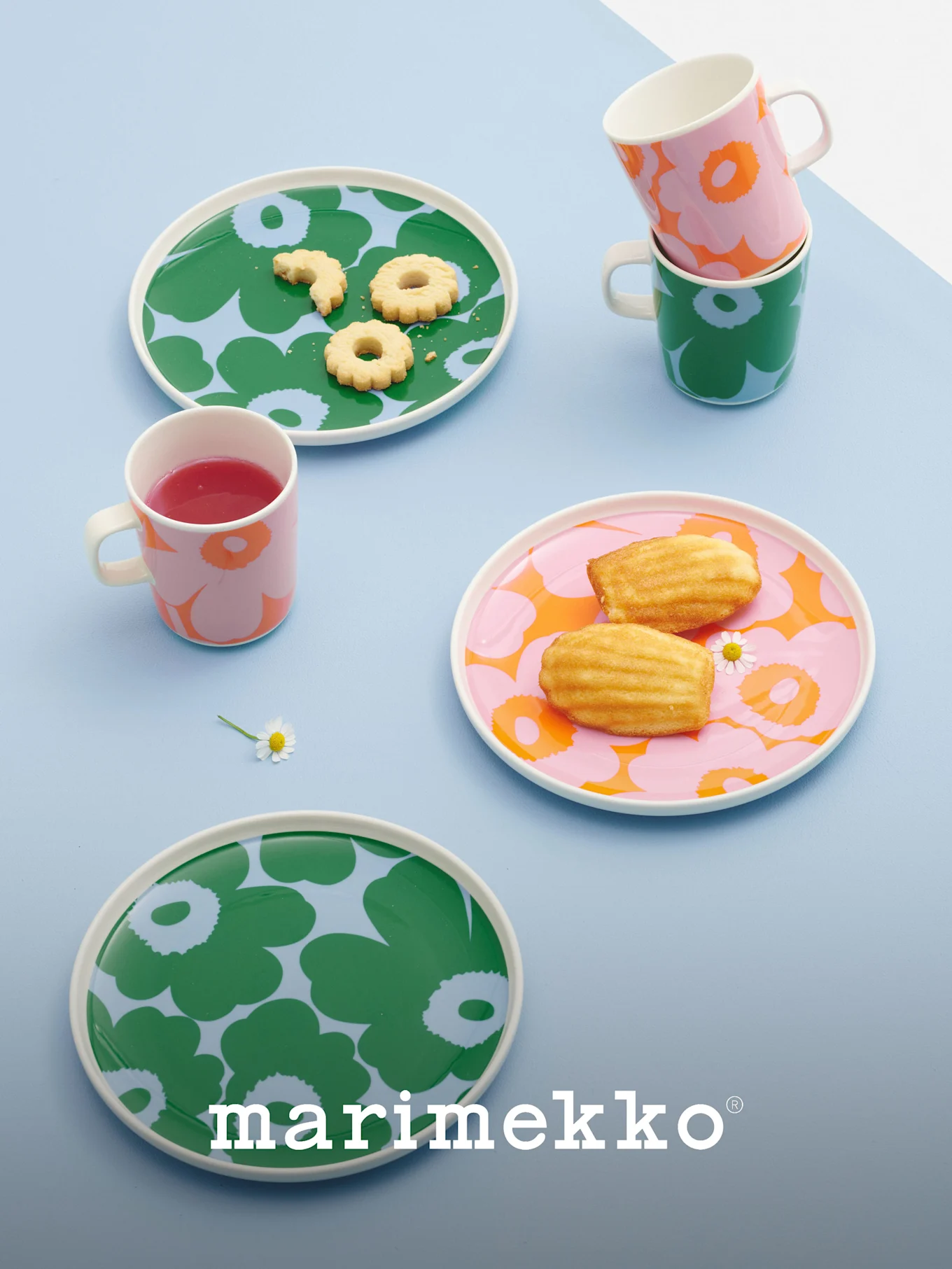 Marimekko tallerkener og krus med dristige blomstermønstre i grøn, pink og orange, indeholdende småkager, madeleines og en drink.