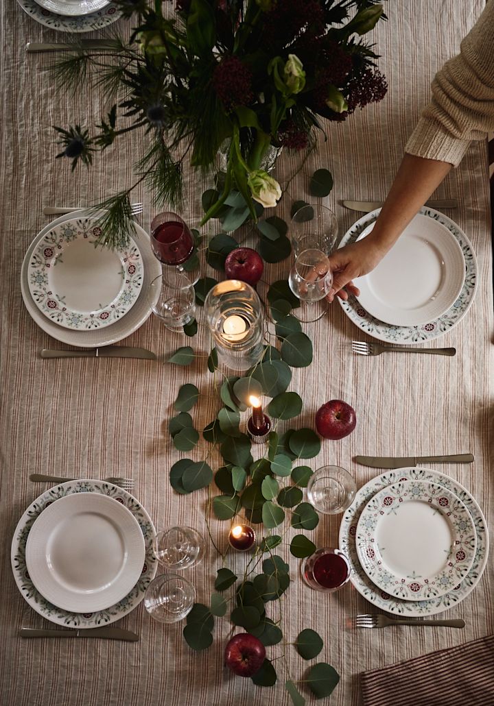 En enkel og elegant idé til juleborddækning fotograferet fra oven med grønne blade og røde æbler som dekoration. 
