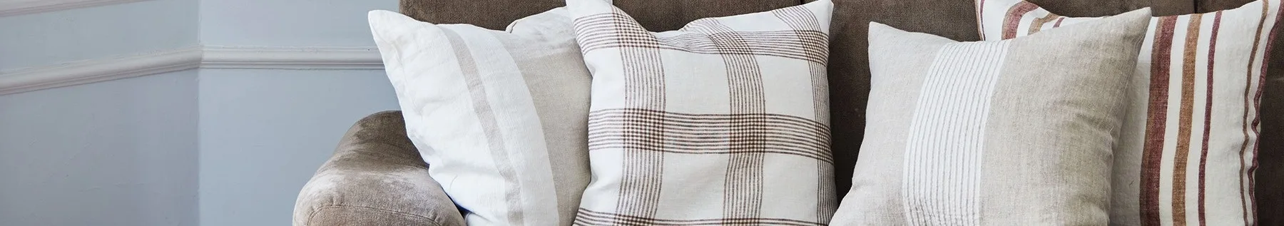 Nærbillede af tre puder på en brun sofa, med hvide, beige og ternede mønstre med brune og røde striber.