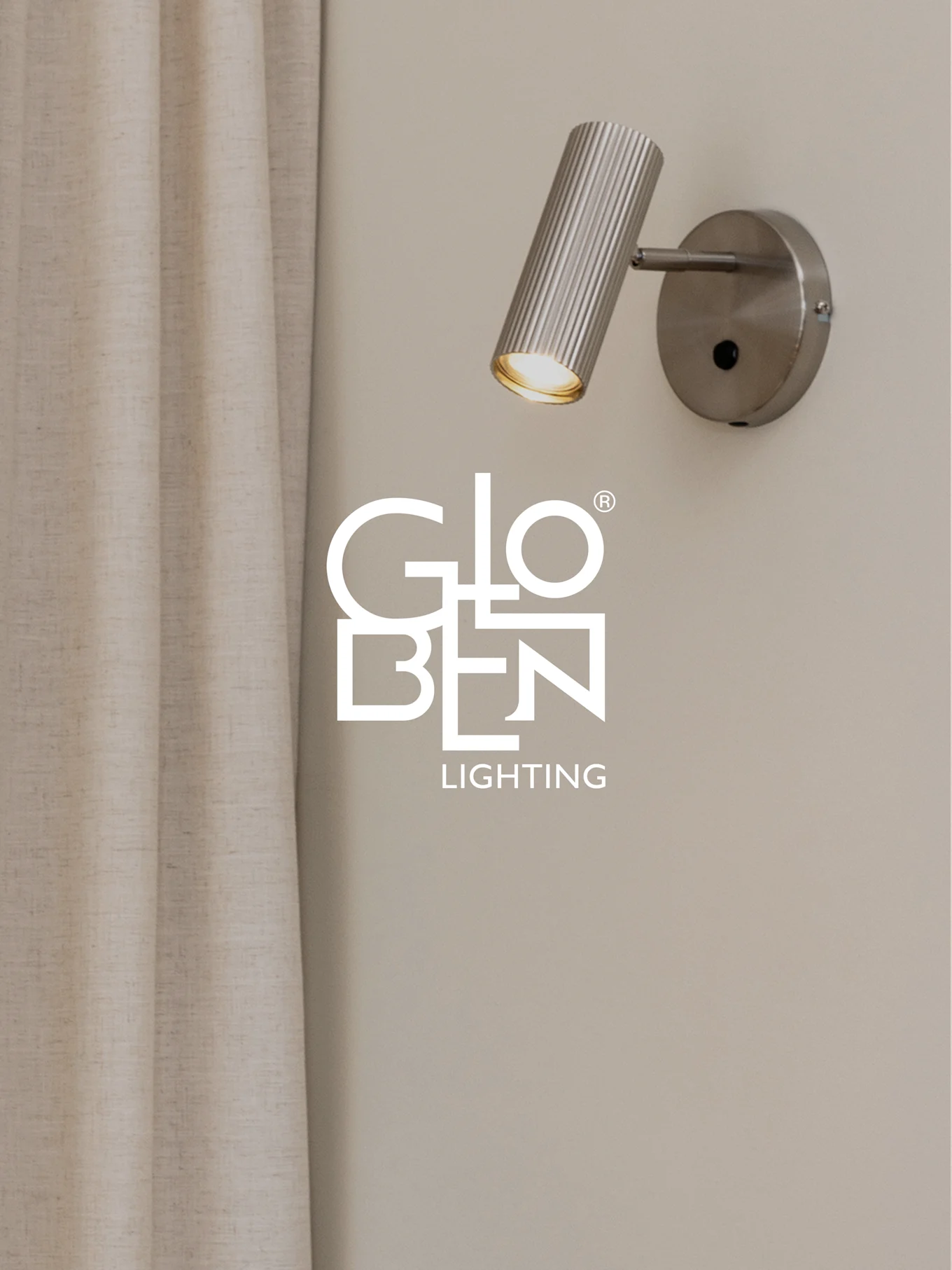 En børstet metal, ribbet vægspotlight med et varmt skær, ved siden af et lyst gardin, med Globen Lighting logoet.