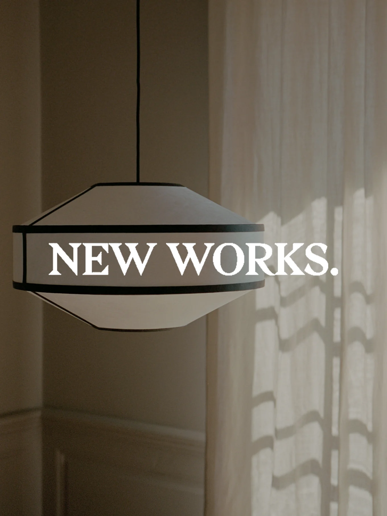 En bred, hvid og mørkkantet pendellampe hænger med teksten 'NEW WORKS.' overlejret. Sollys kaster skygger på et gardin.