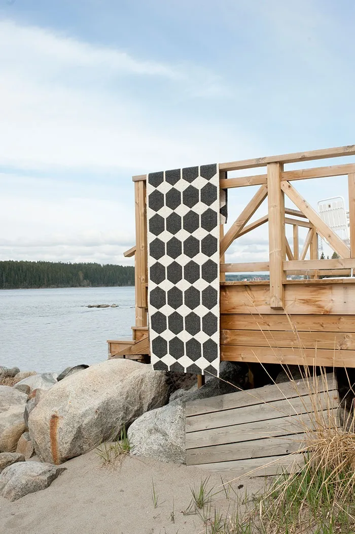 Udendørstæppe: Rengør dit udendørstæppe med jævne mellemrum, og hæng Anna-tæppet fra Brita Sweden i sort, som vist her, til tørre over f.eks. altanrækværket.