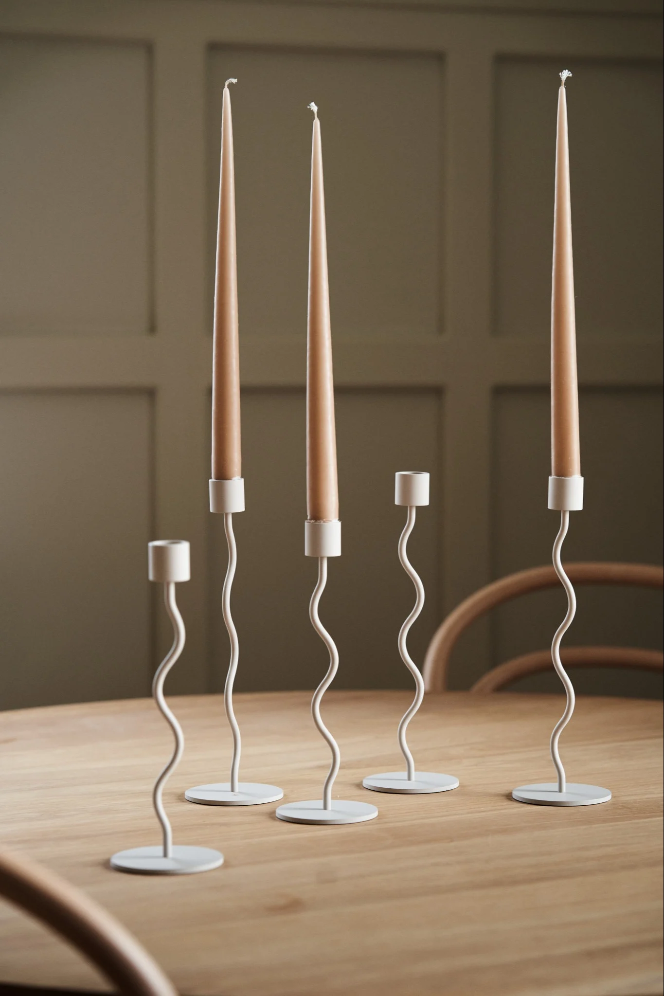 En kollektion af curve lysestagerne i beige fra Cooee Design på et træ spisebord.
