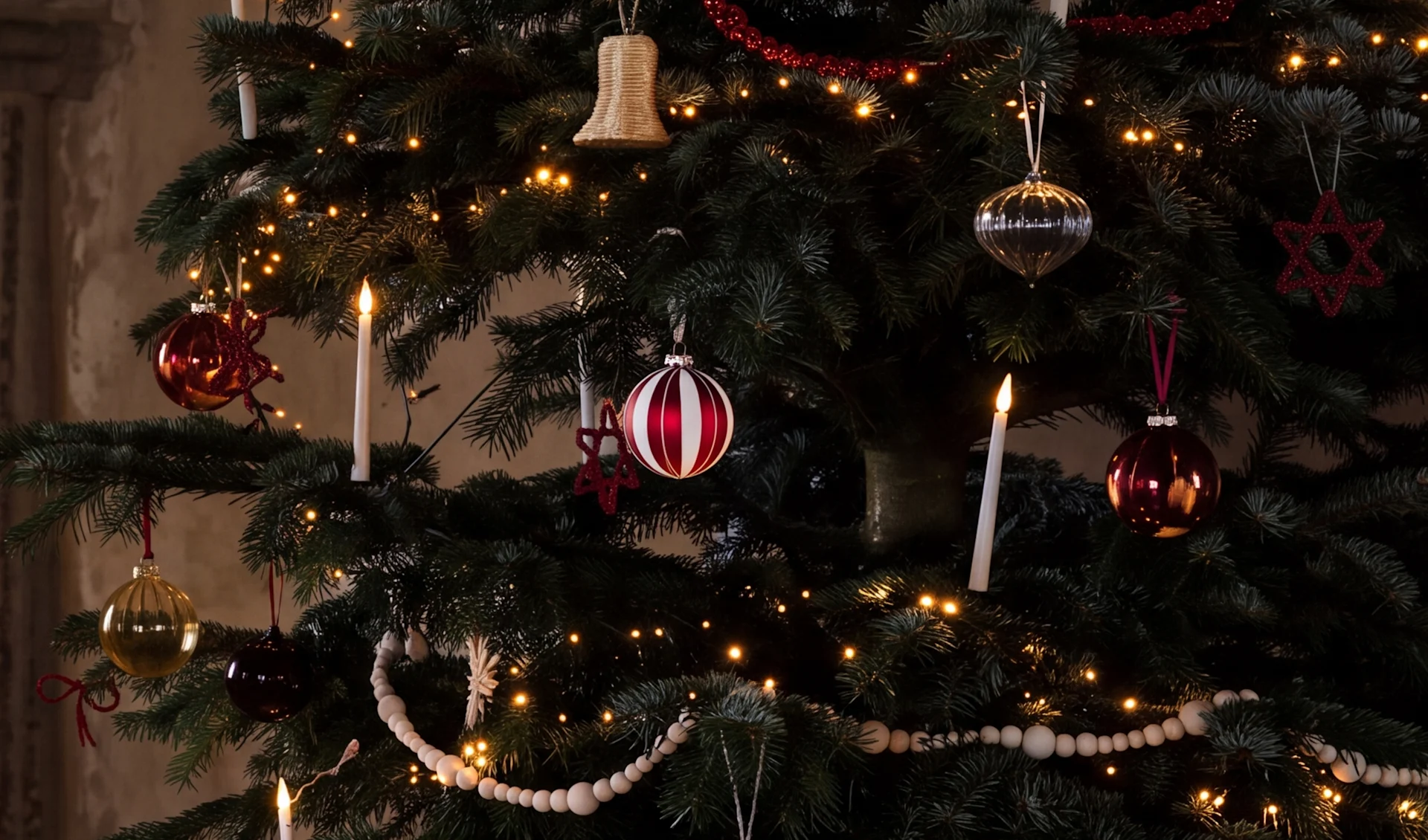 Et pyntet juletræ med varme lys, røde, sølv og guld julekugler, hvide stearinlys og træperlekæder.