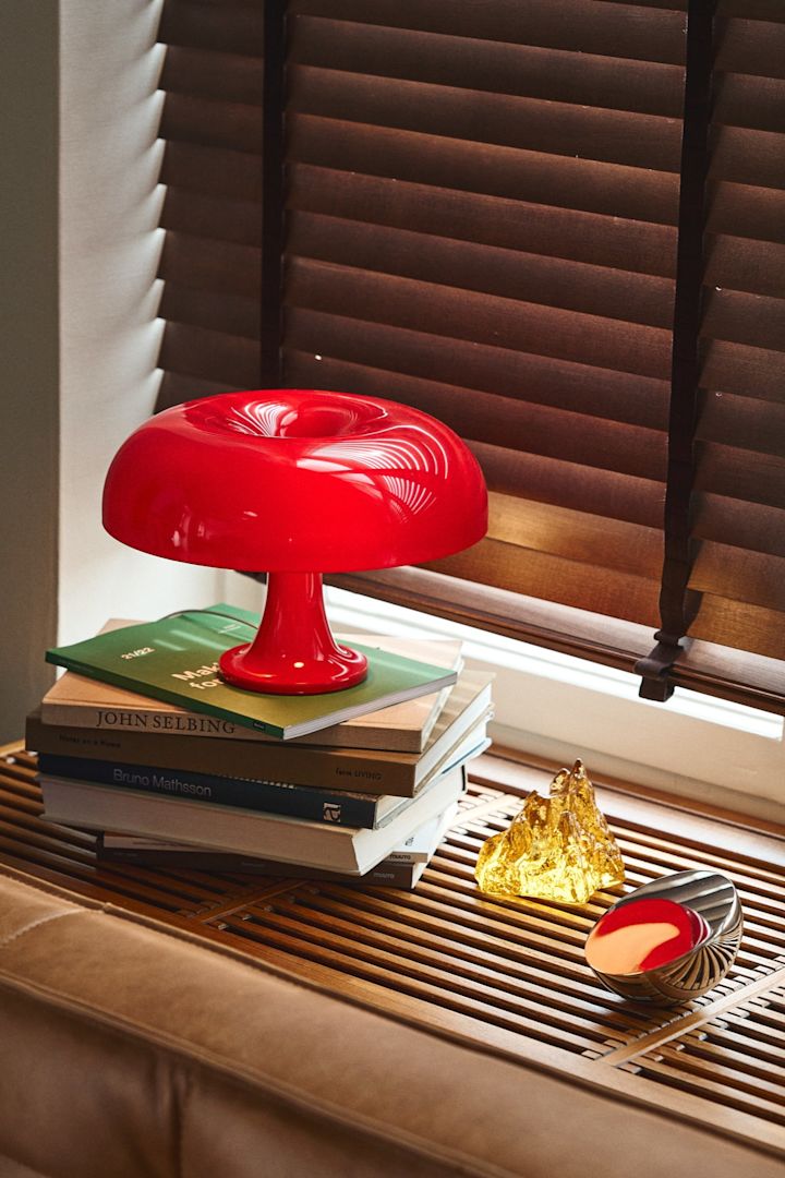 Opdater dit hjem med moderne belysning som Instagram-favoritten Nessino i rød fra Artemide. Her ses den i en vindueskarm af træ med en gul lysestage fra Kosta Boda. 