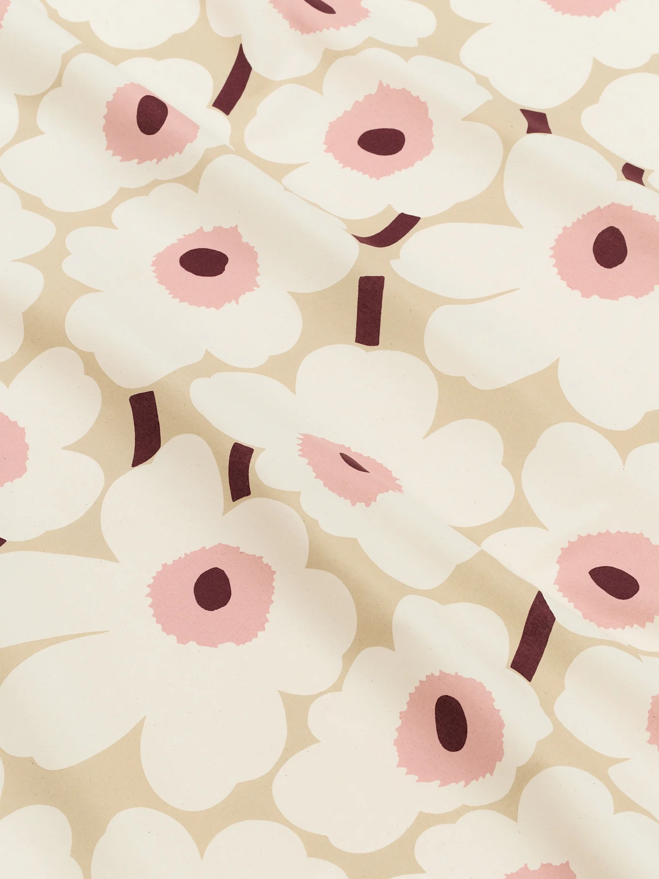 Nærbillede af et lysebeige stof mønstret med store hvide stiliserede blomster med lyserøde centre og mørke bordeaux stængler.