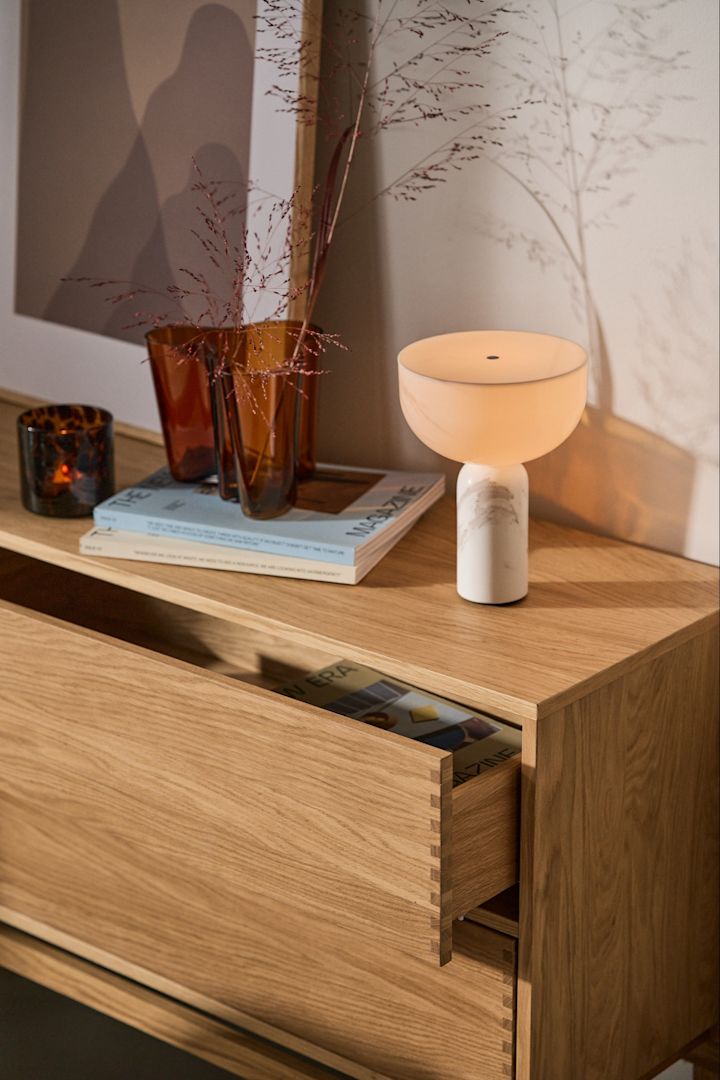 Forny dit hjem med trendy lamper - her ser du den finurlige Ferm Living Vuelta-bordlampe i hvid på en lille træskammel.