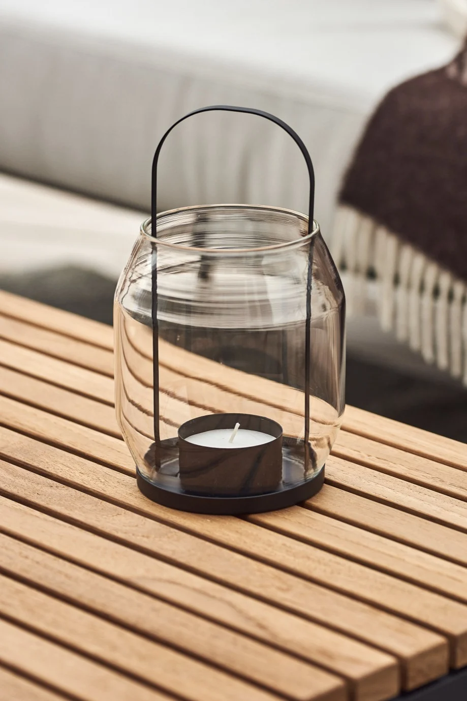 Lanterner og lygter til udendørs brug - her ses en ERNST-lanterne i glas og sort metal, som står på et altanbord af træ.