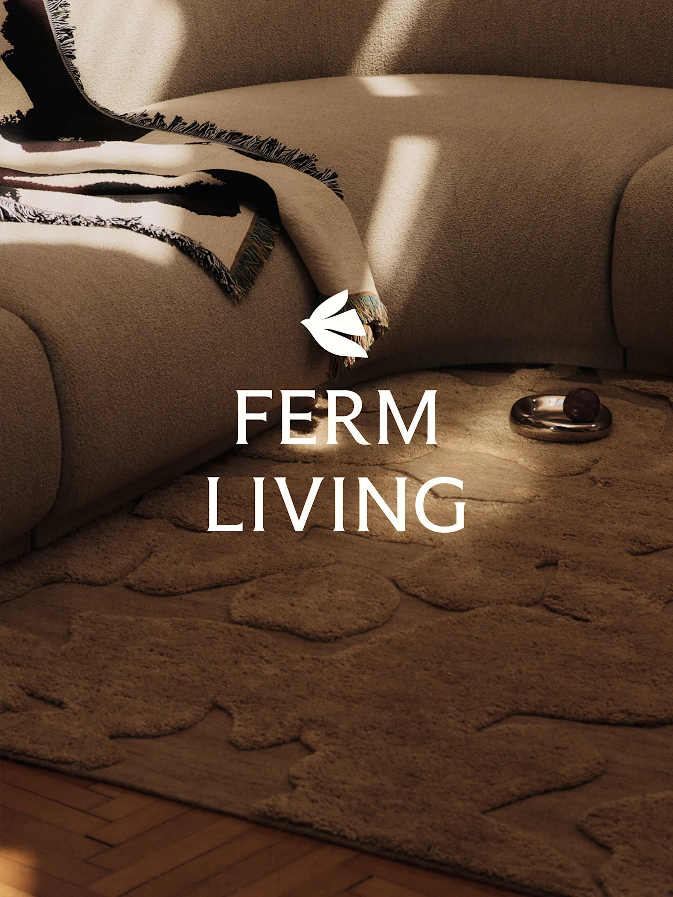 En hyggelig scene med en lysebrun tekstureret sofa, et mønstret tæppe, et brunt tæppe med organiske former og en dekorativ skål.