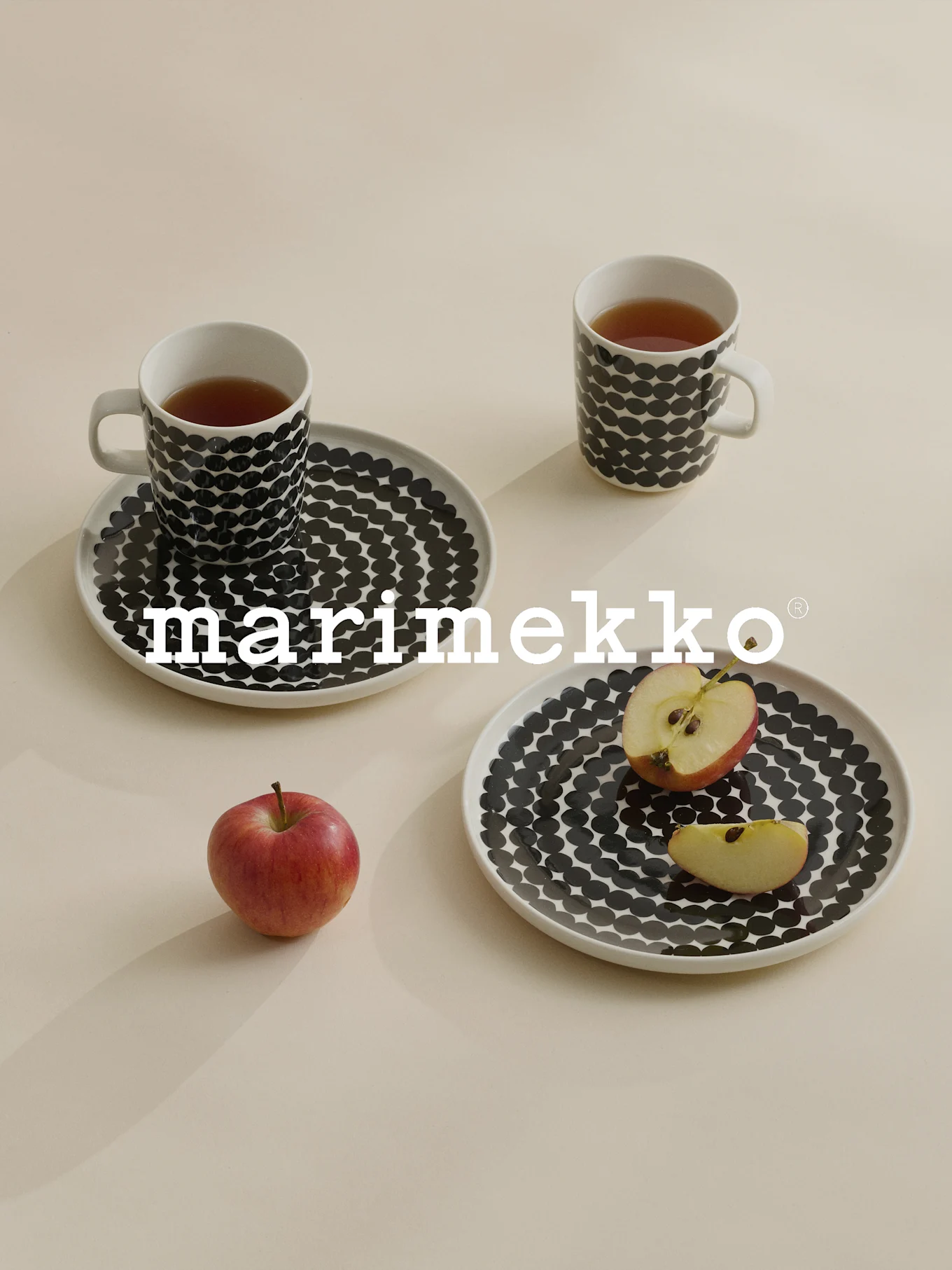 To krus og tallerkener med sorte polkaprikker, te, rødt æble, Marimekko-logo.