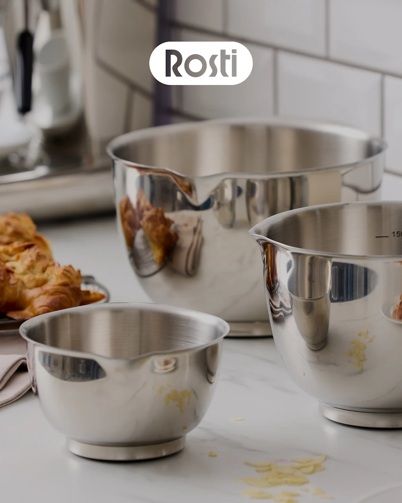Tre Rosti skåle på en disk: en beige skål med en blå stablet ovenpå, begge med låg, og en lille gul skål fyldt med tørrede abrikoser.
