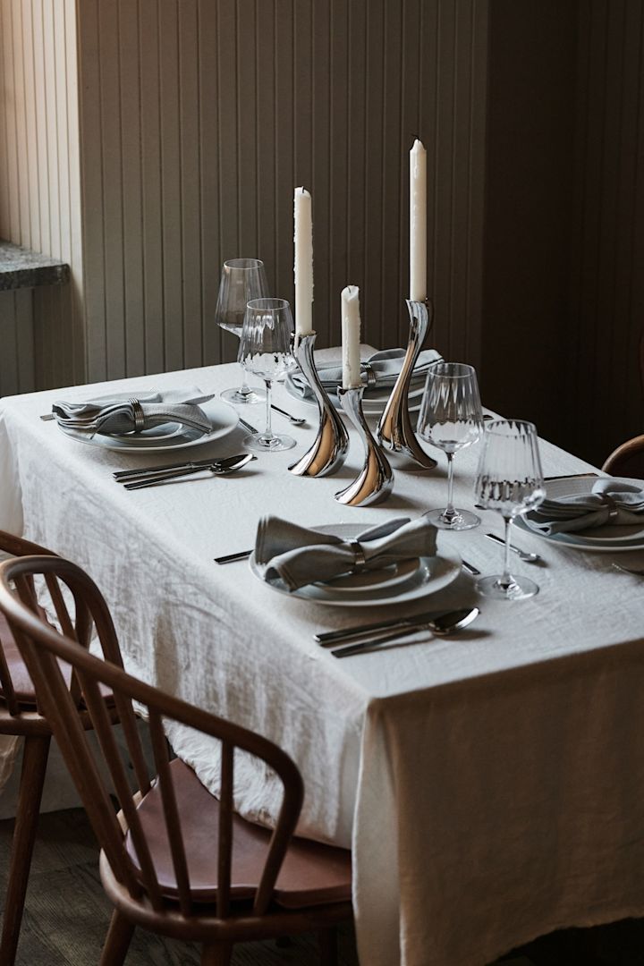 En hvid borddækning med en nystrøget hvid dug og komplimenterende krom detaljer for en borddækning i en restaurantstil derhjemme.