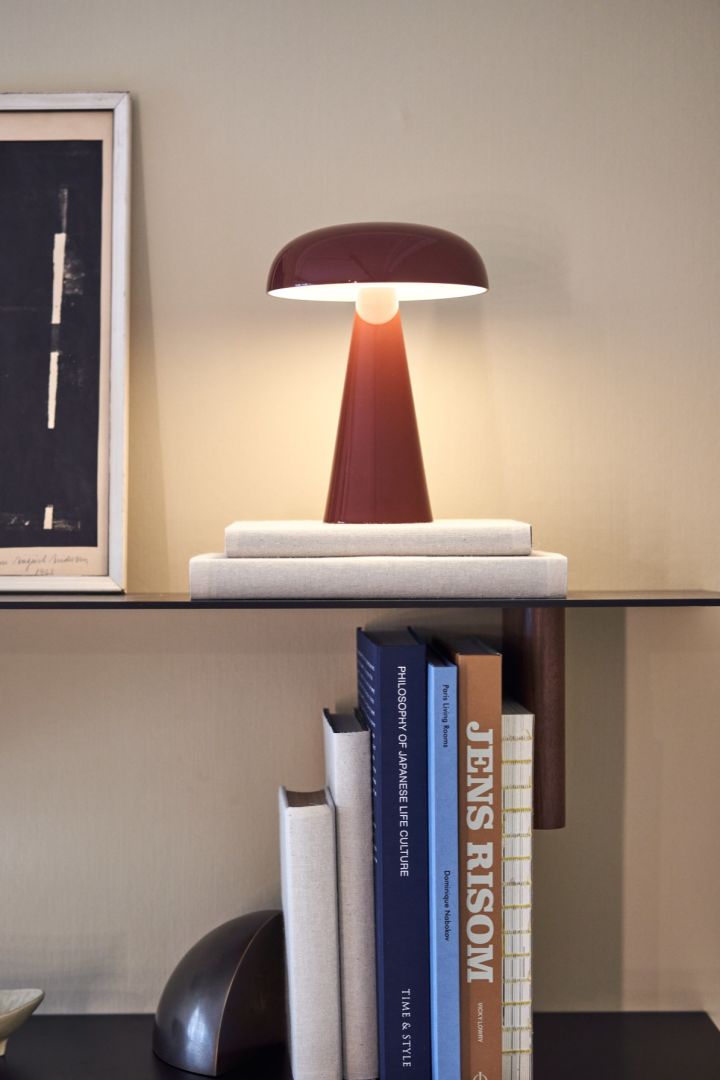 Den trådløse bordlampe fra &Tradition står på en hylde med bøger og en billederamme.