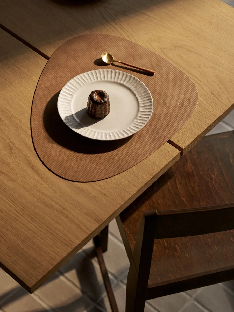 Ovenfra: canelé på hvid tallerken, guldske på brun dækkeserviet på træbord.