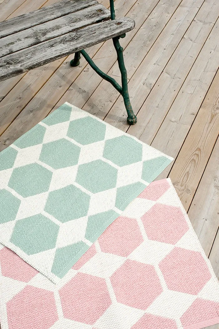 Udendørstæppe: Her ser man det grønne og det pinkfarvede udendørstæppe fra Brita Sweden ligge foran en bænk på en træterrasse.