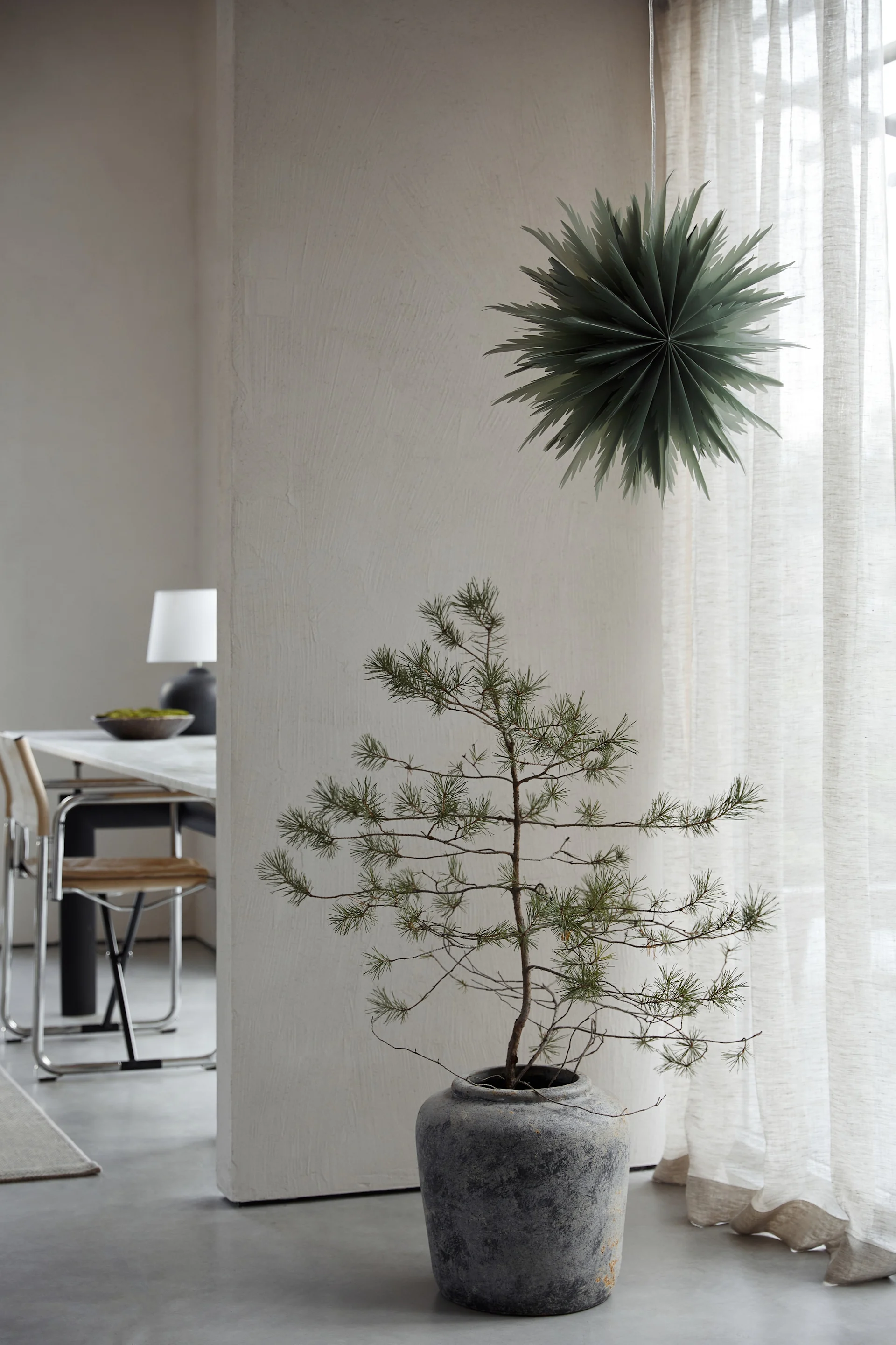 Juletræ med stearinlys, klokker og snefnug ved et skab med en dekorativ vase.