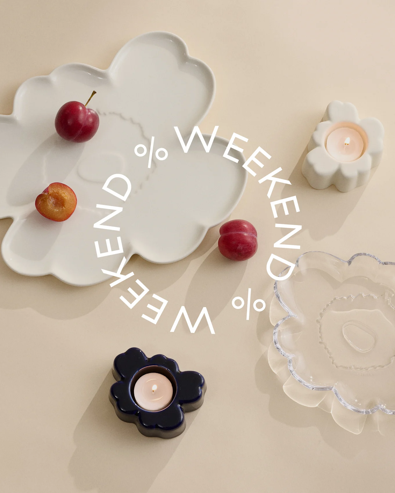 Dekorative tallerkener og lysestager i hvid, blå og klart glas med blommer på en beige baggrund. Hvid tekst siger 'Weekend %'.