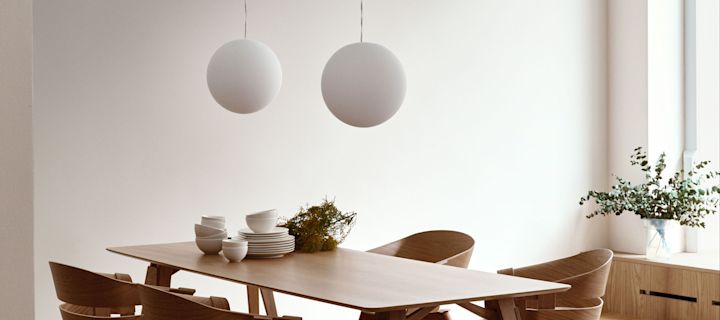 Design House Stockholm Luna lampen der hænger i et par over et træ spisebord.