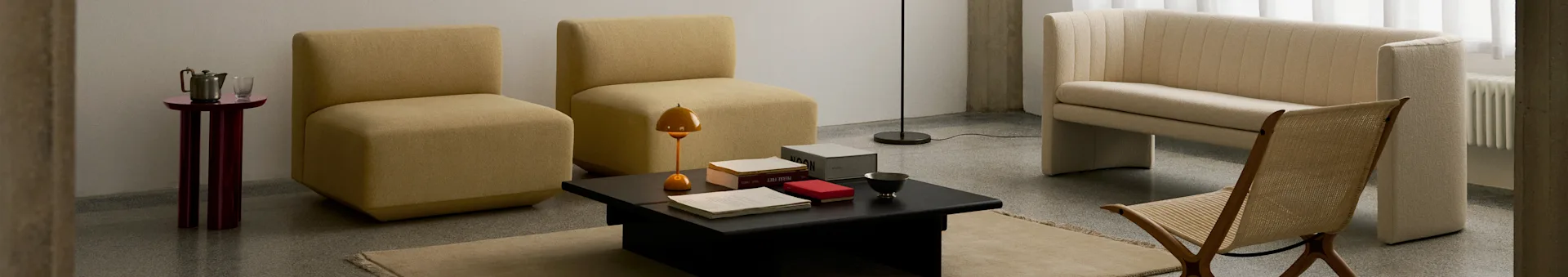 En moderne stue med to sennepsgule armløse stole, et sort sofabord, en cremefarvet ribbet sofa og en flettet træstol.
