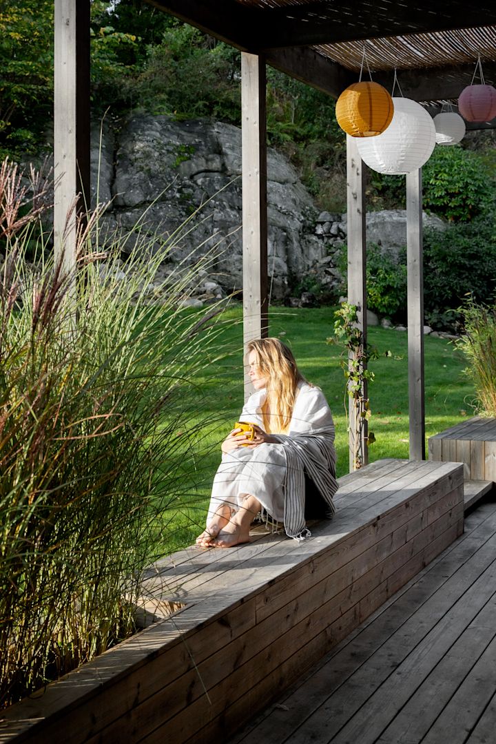 En kvinde sidder ude på en veranda og nyder hendes fika.