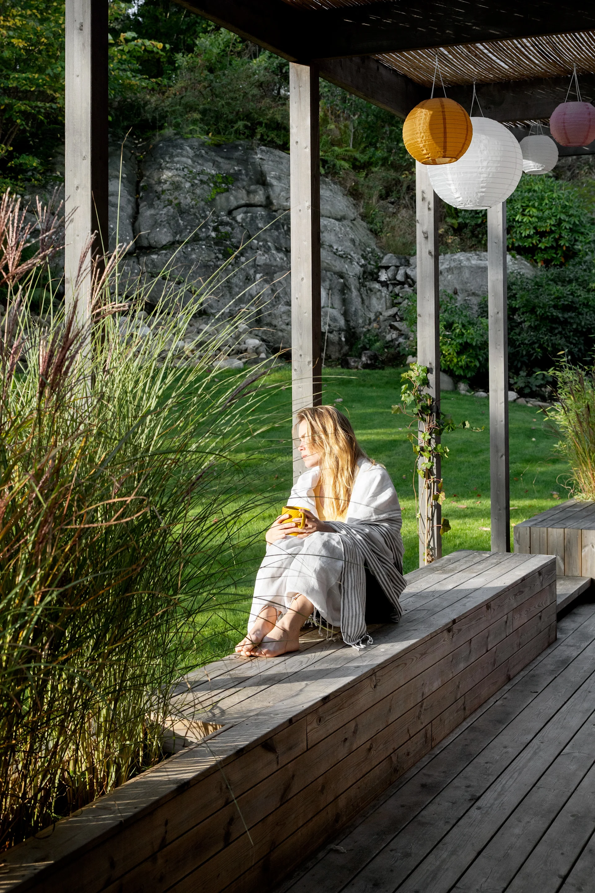 En kvinde sidder ude på en veranda og nyder hendes fika.