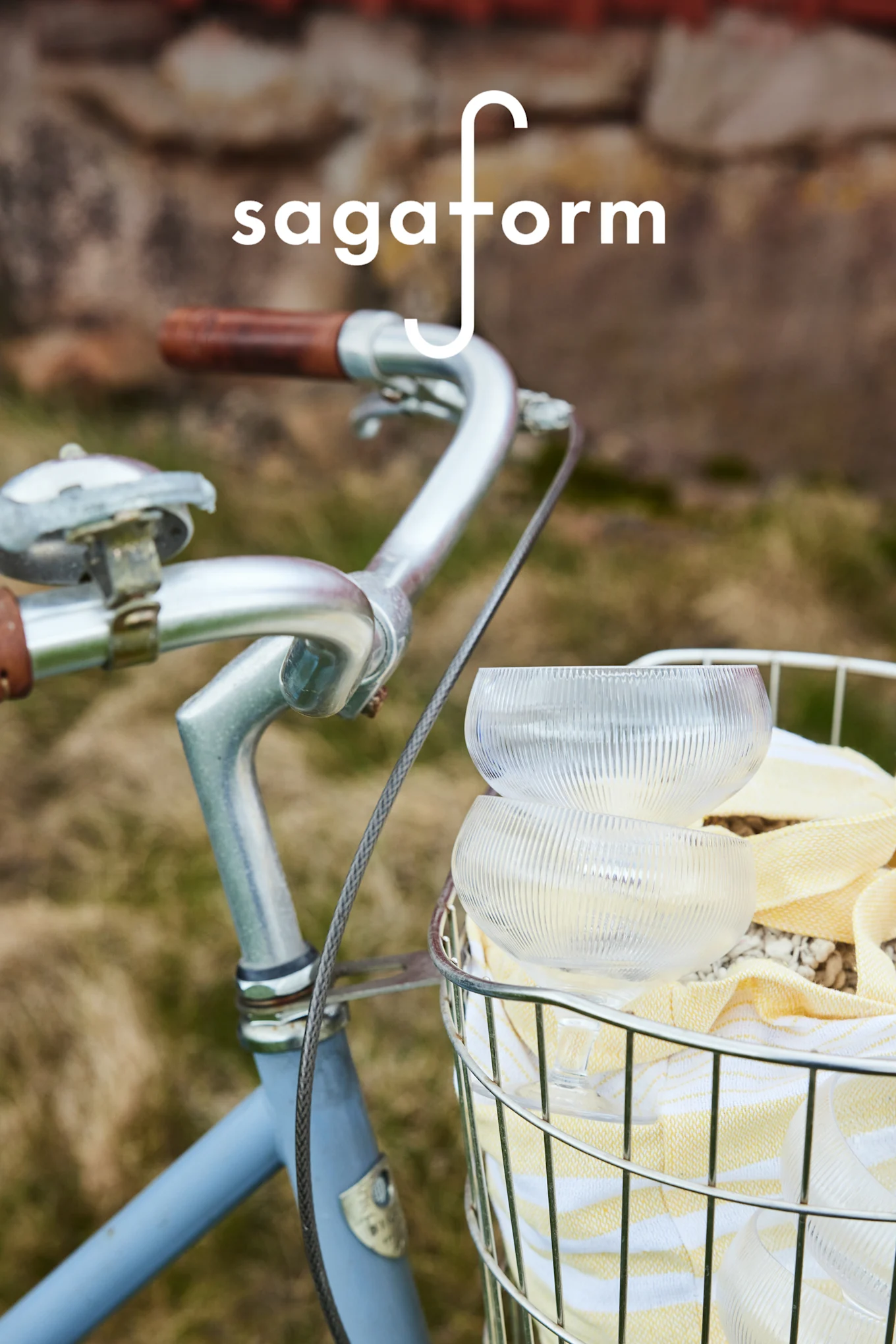 To klare, riflede glasskåle og et gulstribet håndklæde i en cykelkurv. 'sagaform'-logo.