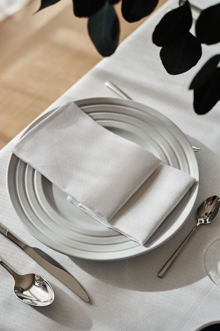 En sprød hvid borddækning med en foldet hvid serviet og hvis dug og hvidt porcelæn fra NJRD.