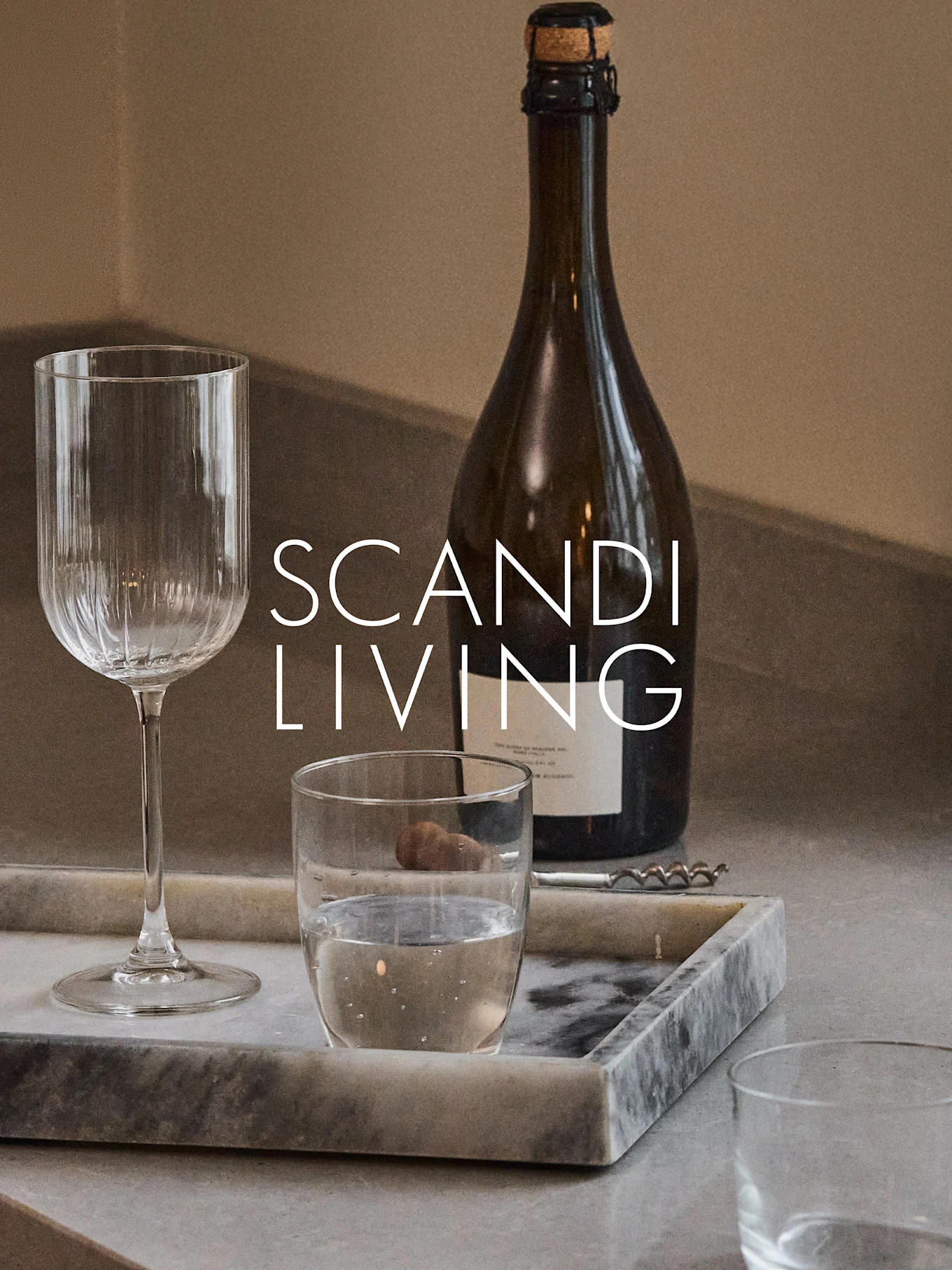 En mørk flaske, et ribbet vinglas, et vandglas og en proptrækker på en marmorbakke med teksten 'SCANDI LIVING'.