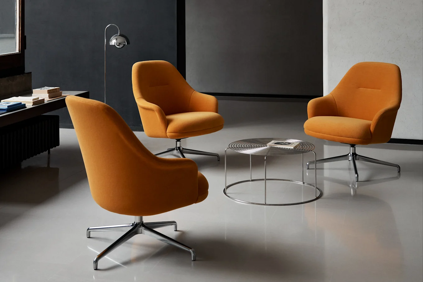 Tre orange drejestole samlet omkring et rundt sofabord i krom i et moderne rum.