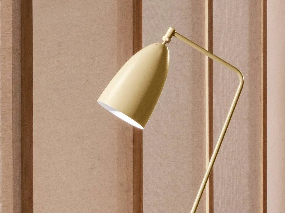 Et nærbillede af en gullig-guld moderne lampe med et konisk hoved vinklet nedad, der udsender lys mod en lysebrun panelvæg.