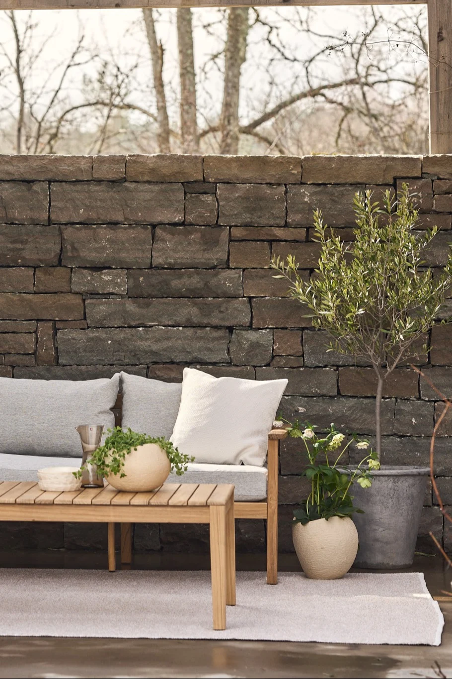 En hyggelig terrasse med et tæppe, en sofa og et lille bord ved siden af mange planter.