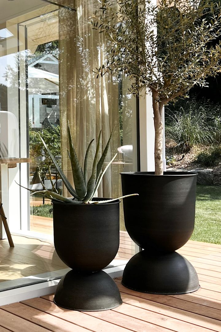 Her ses to af de store Hourglass udendørs krukker fra Ferm Living stående på en terrasse.