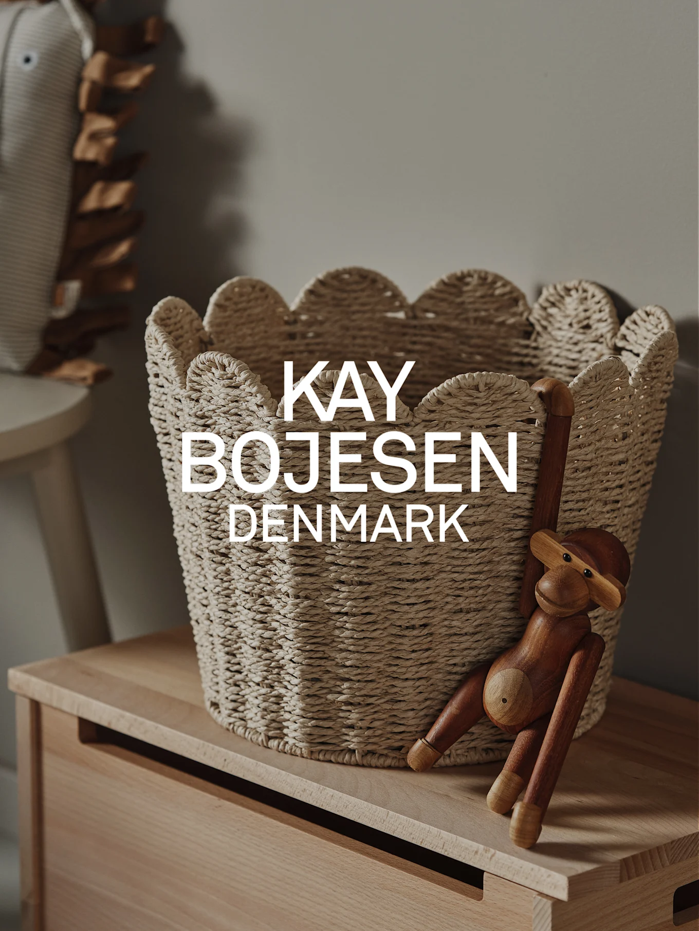En naturlig flettet kurv med bølgede kanter og en træabe-legetøj hængende på et lyst træskab.