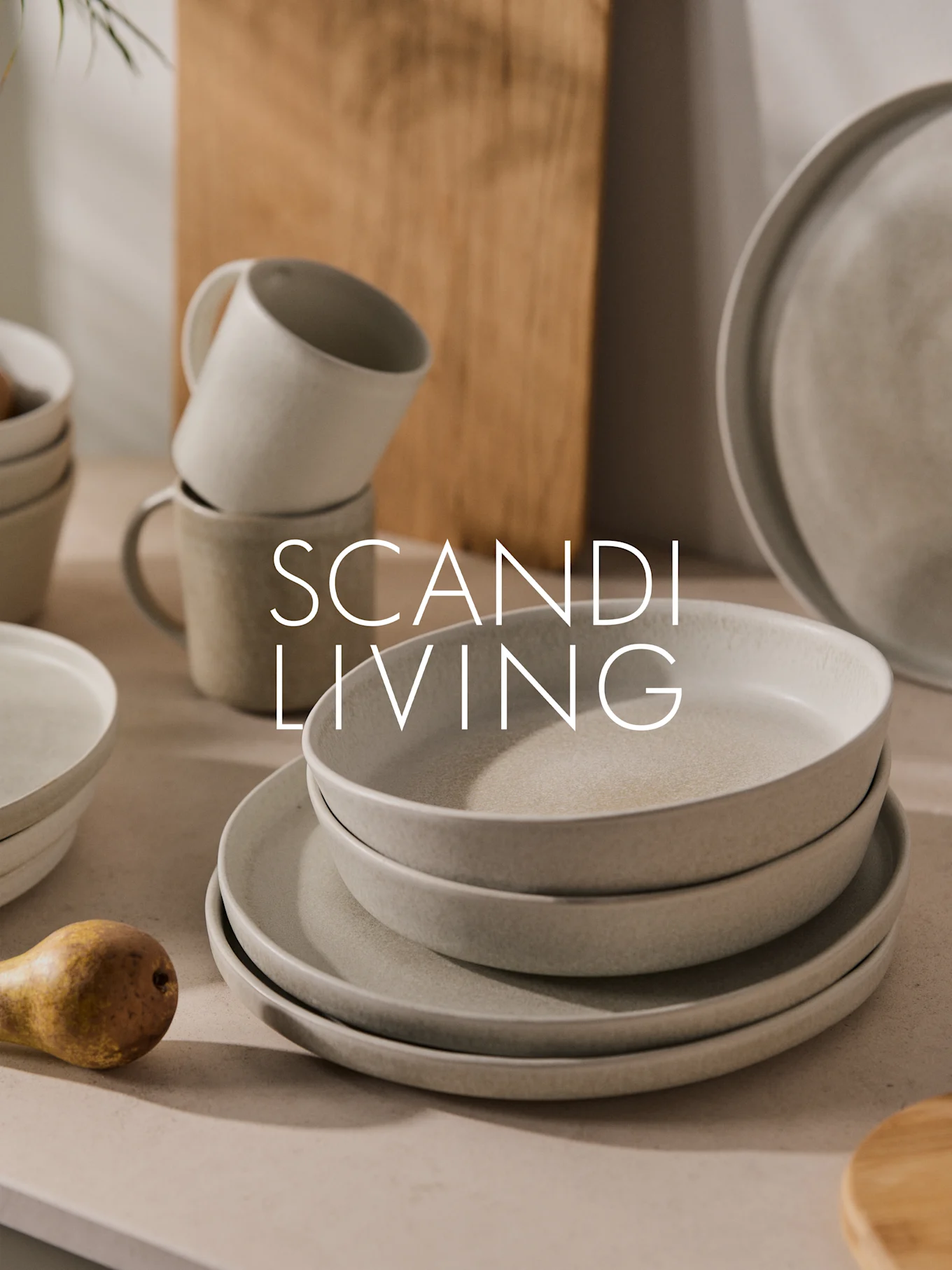 Stabel lyse, spraglede keramiktallerkener, skåle og krus med en pære. Tekst: SCANDI LIVING.