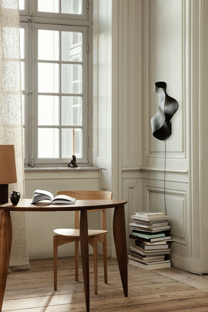 Opdater dit hjem med disse moderne belysningsideer som Oyster-væglampen fra Ferm Living. Her hænger den på væggen over en bunke bøger. 
